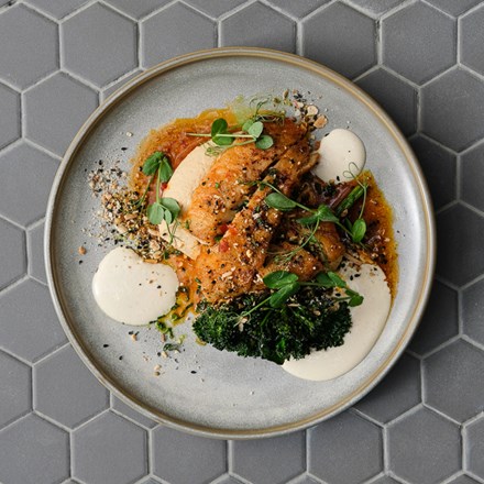 Top view of a pan-seared ōra king salmon dish with roast carrots , dukkah and herb yoghurt served on up a plate.
