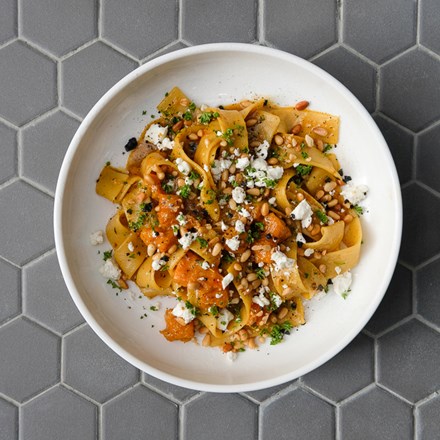 Top view of a pappardelle pasta in a white plate served with pumpkin, spiced butter emulsion, toasted pine nuts, goat’s cheese and parsley 