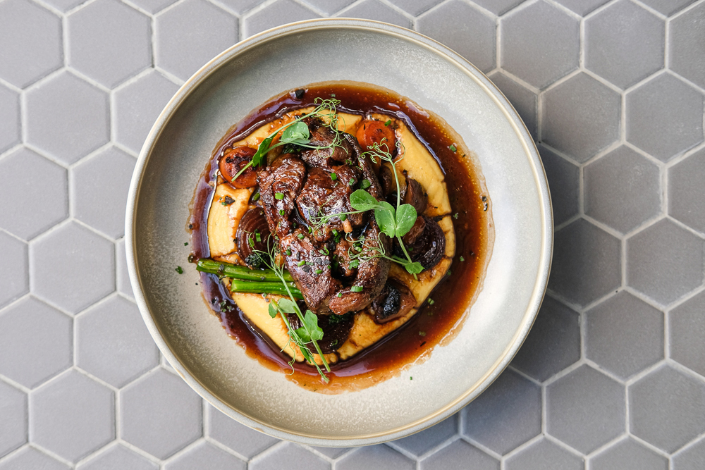 Top view of a lamb dish meal mixed with home made sauce and greens served on a plate.