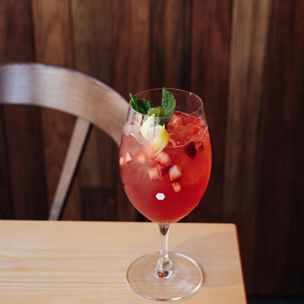 Front view of a red cocktail with strawberry bits, lemon and mint leaves.