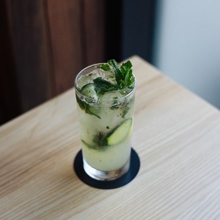 Front view of a cold cucumber mojito drink served on a glass placed on the top of a wood table.