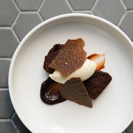 Top view of a dessert dish on a white plate includes chocolate and coffee terrine, almond brittle, and vanilla cream.