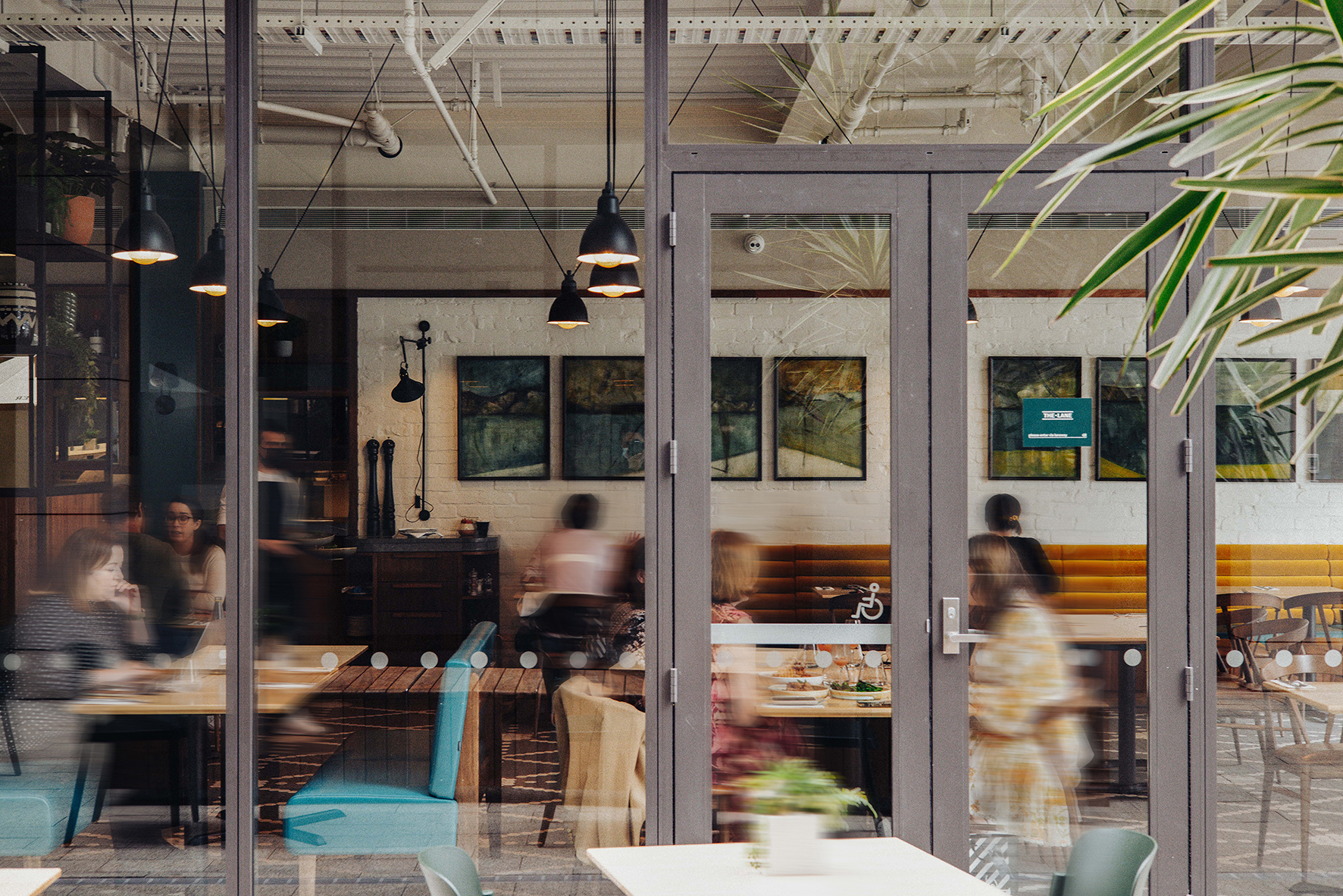 Outside motion blurred front view of a modern restaurant exterior. Huge glass window panels, wooden chairs and table inside with happy customers eating their food.